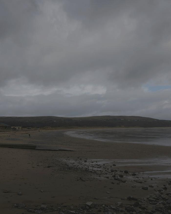 An overcast sky over a quiet bay and low hills