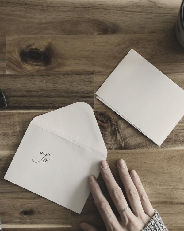 A hand resting beside an envelope and a folded card on a wooden table