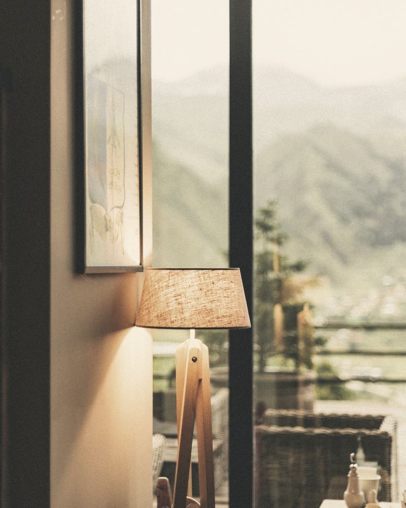 A lamp-lit room with a tall window over misty mountains